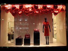 a window display with red hearts hanging from it's sides and two mannequins in front