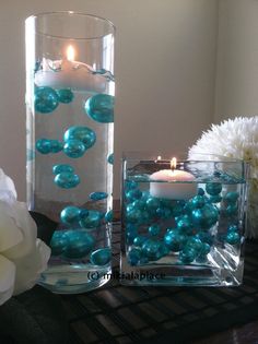 two clear vases filled with blue pearls and a lit candle