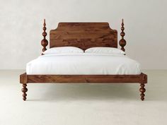 a wooden bed frame with white sheets and pillows on the headboard, in front of a plain wall