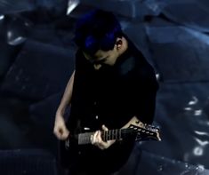 a man with blue hair playing an electric guitar