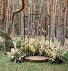 an outdoor ceremony area with flowers and greenery on the ground, surrounded by trees