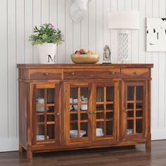 a wooden sideboard with glass doors and drawers on top in a white walled room