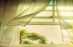 an open window with white curtains and green trees in the backgroung area