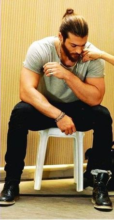 a man sitting on top of a white chair next to a wooden wall and holding his hand near his face