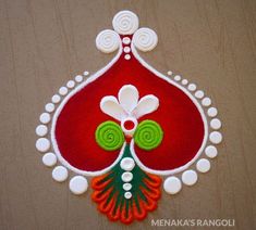 a red and green decoration with white circles on the bottom is hanging from a wooden wall