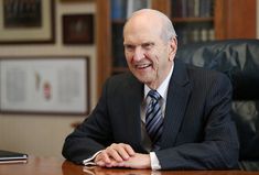 an older man in a suit sitting at a desk with his hands on the table