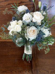 a bouquet of white roses and greenery on a wooden table in front of a mirror