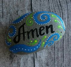 a rock with the word amen painted on it sitting next to a gray sweater