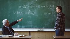 two people standing in front of a blackboard with writing on it and one person pointing at the board