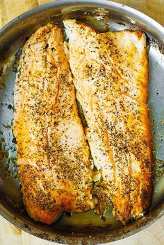 two fish fillets in a skillet on a wooden table with seasoning sprinkles