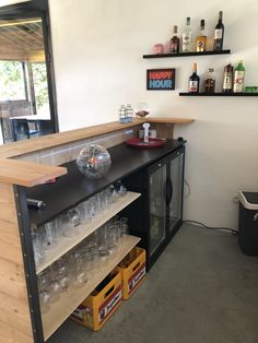 an empty bar with wine glasses and bottles on the shelf next to it in front of a mirror