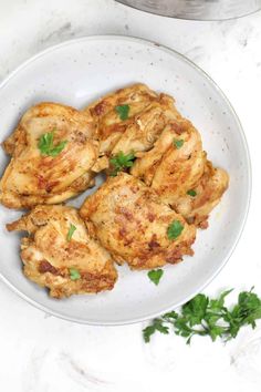 three pieces of chicken on a white plate with parsley garnishes next to it