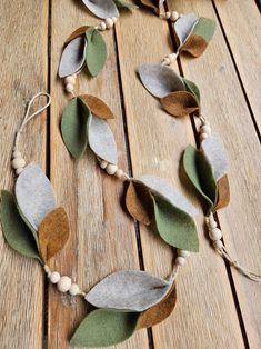 a necklace made out of felt leaves and beads on a wooden table with white beads