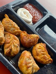 there are several pastries in the tray with dipping sauces on the other side