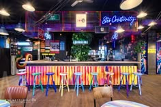 a brightly colored bar with stools and tables in front of it, surrounded by neon lights