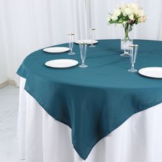 the table is set with white plates and flowers in vases on top of it