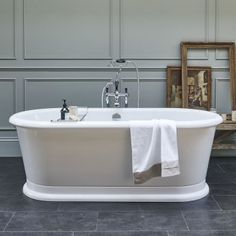 a white bath tub sitting in a bathroom next to a wooden table and framed pictures