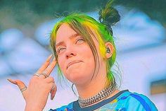 a woman with green hair and piercings holding her finger up to her face while making a peace sign