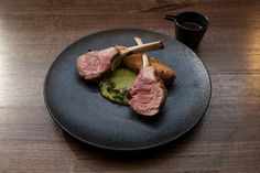 a black plate topped with meat and broccoli on top of a wooden table