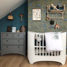 a baby's room with blue walls and green wallpaper, white crib in the foreground