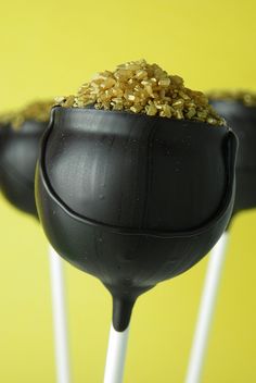 two black cake pops with gold sprinkles on them, sitting on top of each other