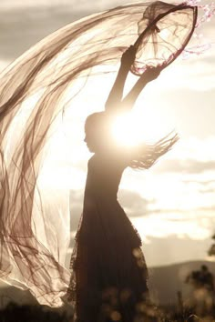 a woman holding a tennis racquet on top of her head in front of the sun