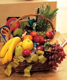 a basket filled with lots of fruit on top of a wooden table next to a box of chocolates