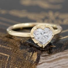 a heart shaped diamond ring sitting on top of an old book with gold trimming