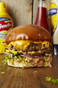 a hamburger sitting on top of a wooden table next to ketchup and mustard