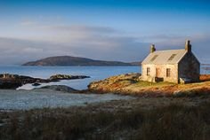 an old house sitting on top of a rocky hill next to the ocean with mountains in the background