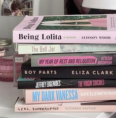 a stack of books sitting on top of a white table next to a pink lamp