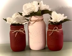 three red mason jars with white flowers in them