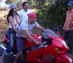 three people standing next to a red motorcycle