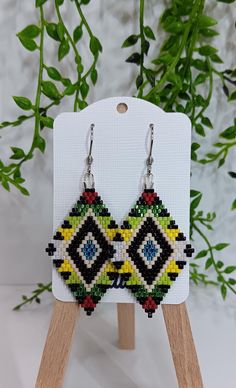 a pair of beaded earrings sitting on top of a wooden stand next to a plant