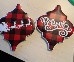 two red and black plaid christmas ornaments with santa on the sleigh, believe and reindeer