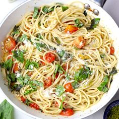 a white bowl filled with pasta, tomatoes and spinach sprinkled with parmesan cheese