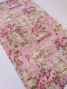 a pink floral table cloth with teapots and roses on it, sitting on a bed