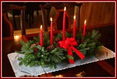 a christmas centerpiece with red candles and pine cones on a lace doily in front of a dining room table