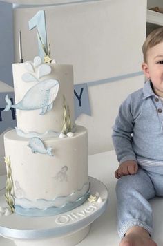 a baby sitting in front of a cake with dolphin decorations on it and the first one next to it