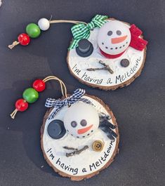 two snowman ornaments are hanging on wood slices