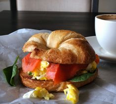 a croissant sandwich sitting on top of a table next to a cup of coffee