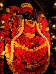 the statue is covered with flowers and candles in front of some lit candles on the wall