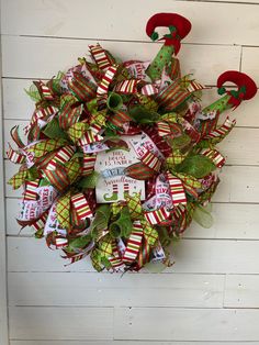 a christmas wreath hanging on the side of a white wall with green and red ribbons