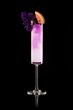 a tall glass filled with purple liquid and garnished with an orange slice