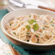 a white bowl filled with pasta and sauce on top of a blue table cloth next to a fork