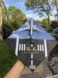 a hand holding up a graduation cap with an airplane on it and the words ba, economics