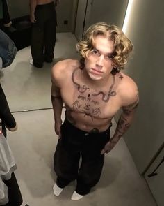 a man with tattoos on his chest standing in front of a mirror and looking at the camera