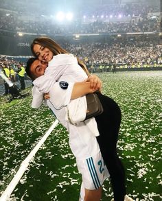 a man and woman hug on the field at a soccer game in front of an audience