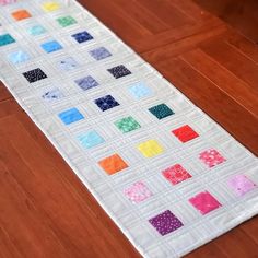 a quilted table runner with different colored squares on the top and bottom, sitting on a wooden floor