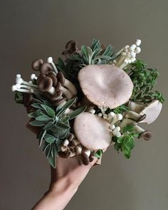 a person holding a bouquet of flowers with mushrooms and leaves on it in their hands